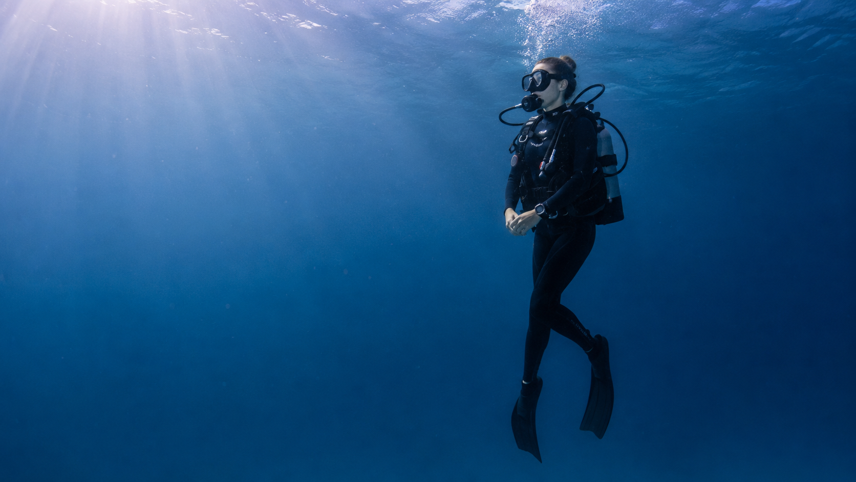 A diver gliding underwater — blue water and shafts of light
